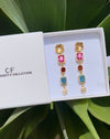 Colorful earrings in a white box with 'CF' branding, set against a green leafy background.