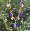 Gold necklace with blue and white pendant against a blurred green background