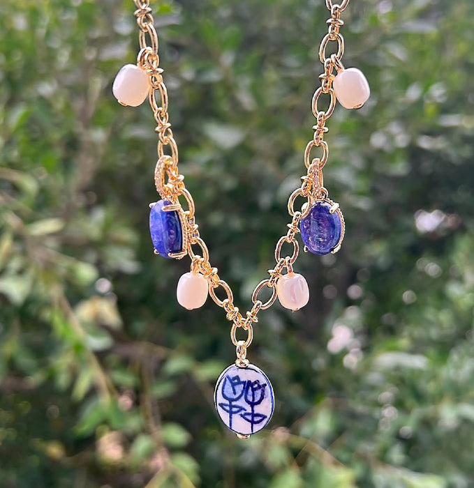 Gold necklace with blue and white pendant against a blurred green background