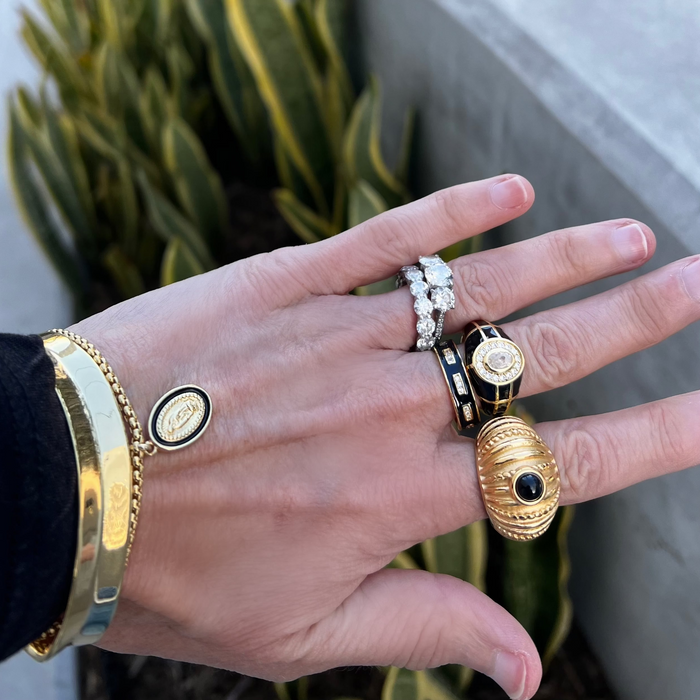 Hand wearing multiple gold and diamond rings with a blurred plant background