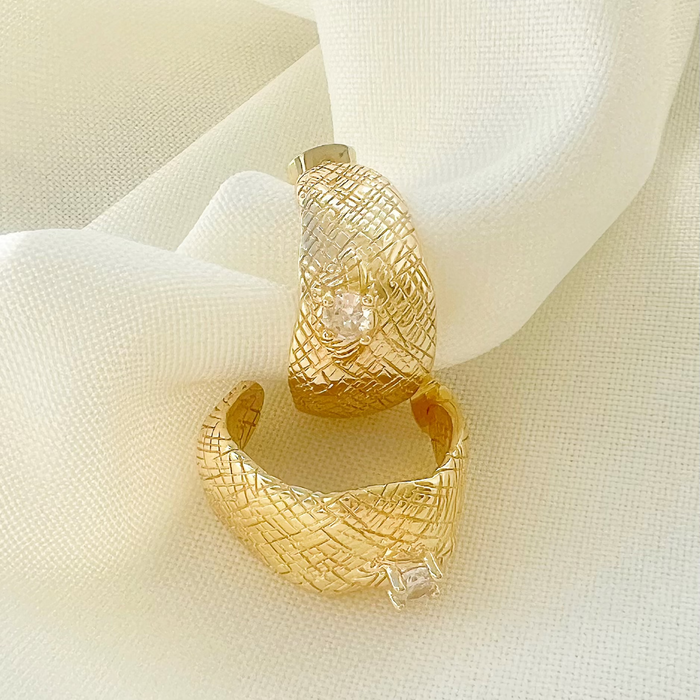 Gold hoop earrings with textured design and embedded diamonds on a white fabric background