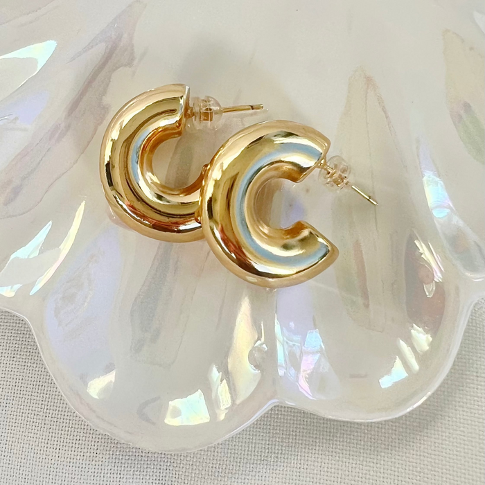 Gold hoop earrings on a white shell background