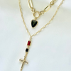 A layered gold necklace set displayed on a white fabric background. The top layer features a gold paperclip chain with a shield-shaped dark green stone pendant.