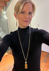 Woman wearing a black turtleneck and gold necklace indoors.