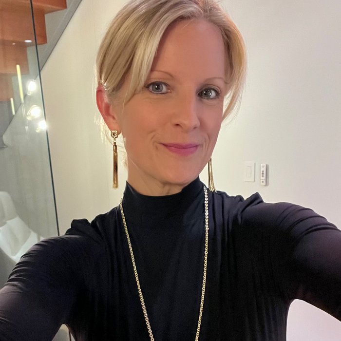 Woman wearing a black turtleneck and gold necklace indoors.