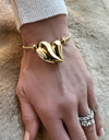 Gold bracelet with a heart-shaped clasp on a wrist against a soft, neutral background