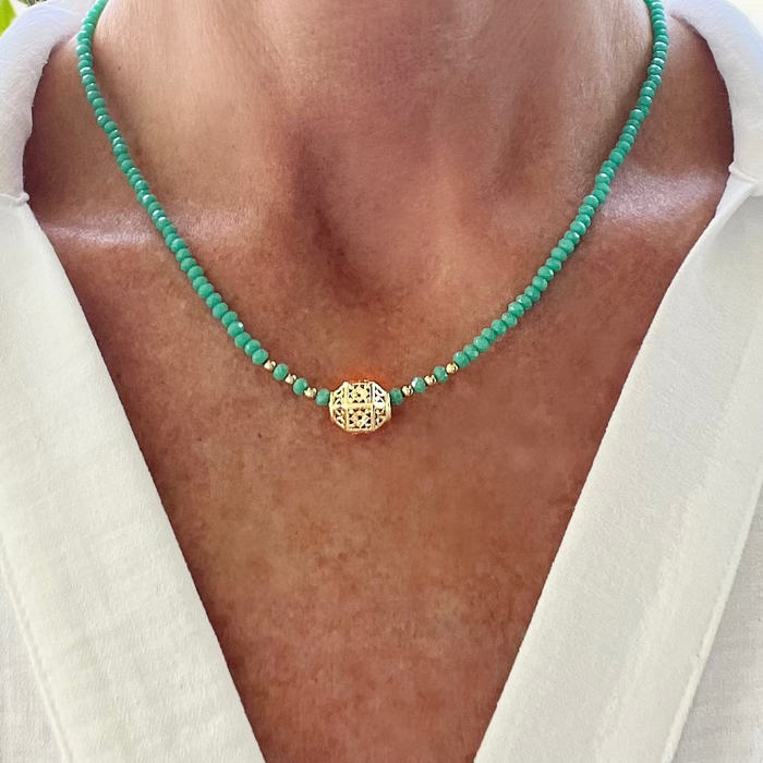 A person wearing a white shirt showcasing a boho beaded necklace with green and gold colors.