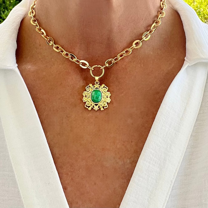A gold-filled necklace with oval chain links and a round rope style connector, featuring a green gemstone pendant, displayed on a person wearing a white shirt.