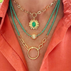 Necklace with green beads and gold chains on a person wearing an orange shirt.