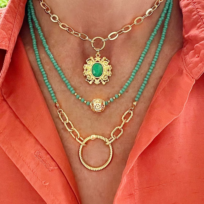 Necklace with green beads and gold chains on a person wearing an orange shirt.