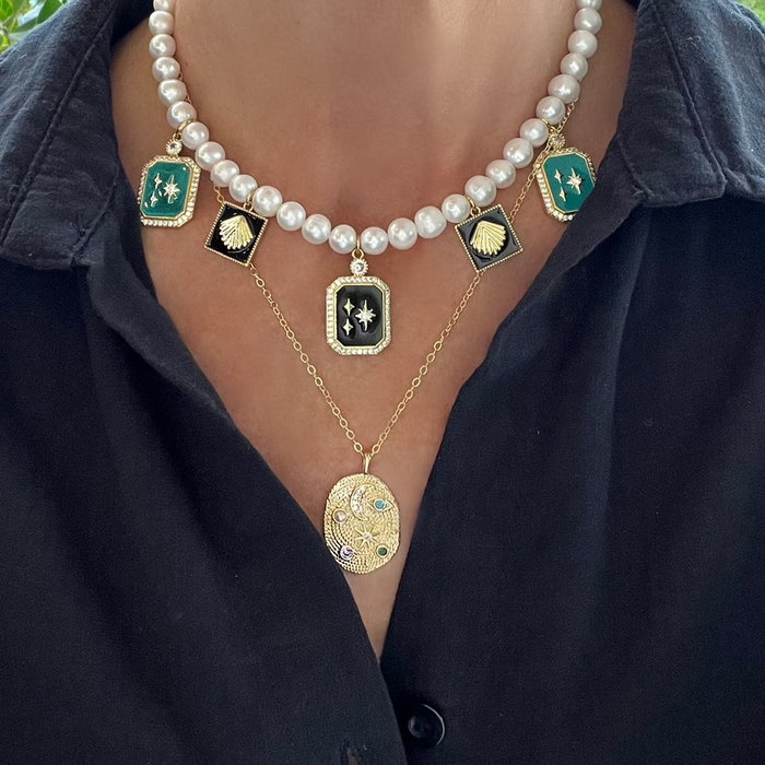 Necklace with pearls and decorative pendants on a person wearing a black shirt.