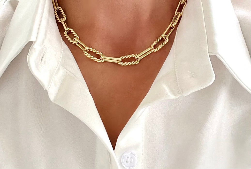 Gold chain necklace worn by a person wearing a white shirt.