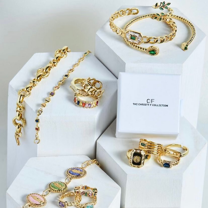 Gold jewelry set including necklaces, bracelets, and rings on white hexagonal stands with 'CF' branding.