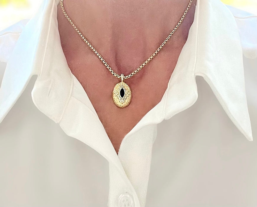 Gold necklace with a pendant worn by a person in a white shirt.