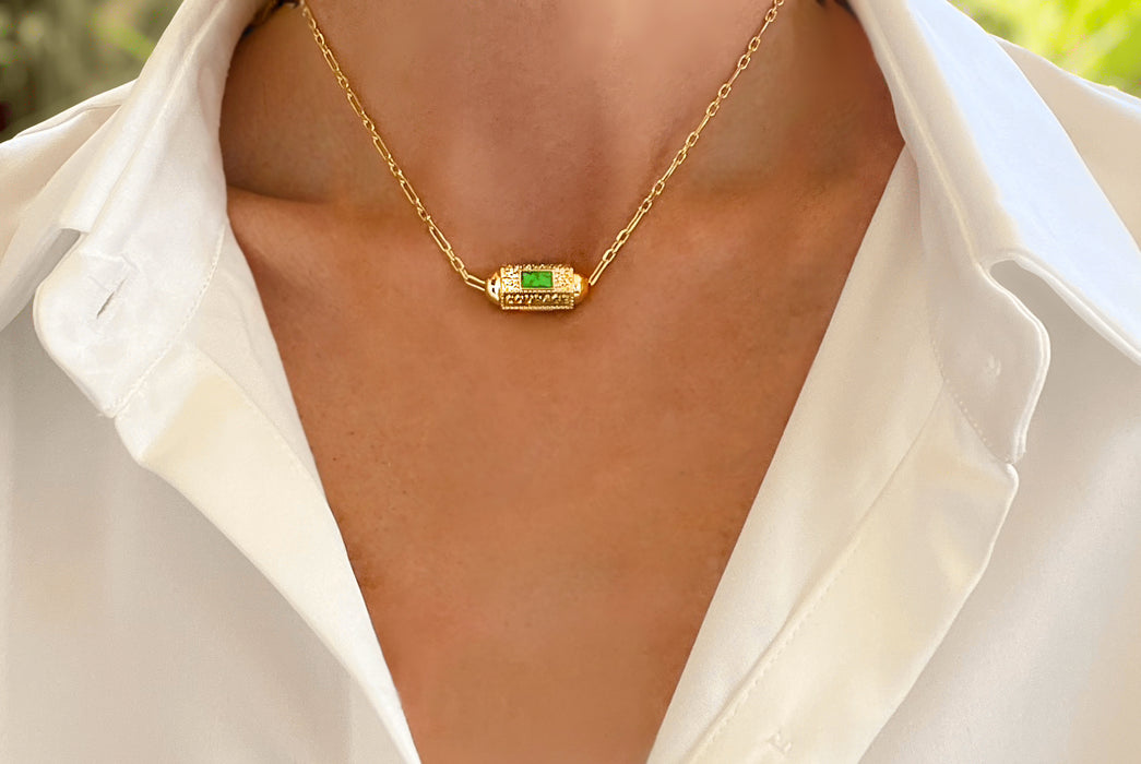 Gold necklace with a green gemstone on a person wearing a white shirt.