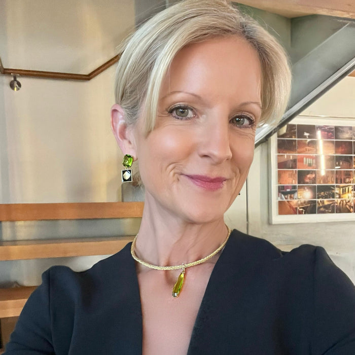 Woman wearing a black outfit with a gold necklace and earrings indoors.