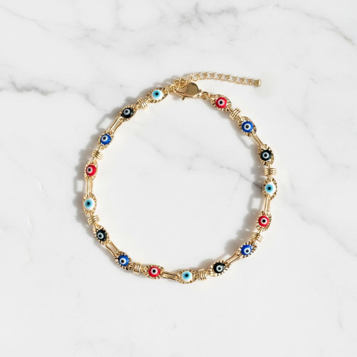 Gold anklet with colorful eye-shaped beads on a marble background
