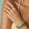 Close-up of a person's arm wearing gold jewelry with a blue gemstone on a neutral background