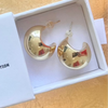 A pair of gold crescent-shaped hoop earrings displayed inside a white jewelry box on a light wood surface.