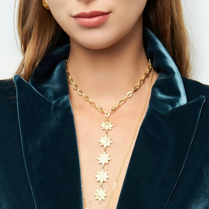 A person wearing a gold-filled necklace with a round chain and sunburst connectors featuring clear center gemstones.