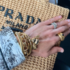 Hand holding a woven Prada bag with gold jewelry