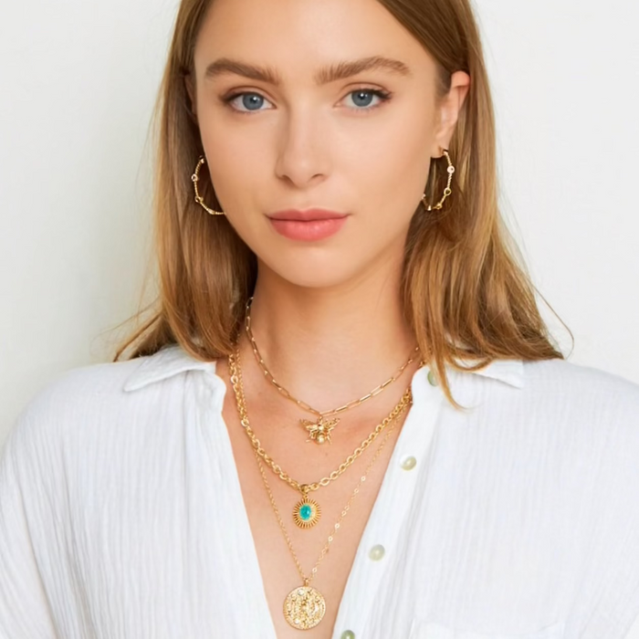 Woman wearing gold jewelry including necklaces, earrings, and bracelets on a white background