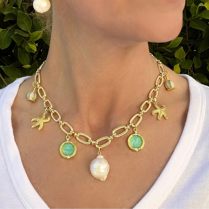 Gold necklace with charms worn by a person against a green leafy background