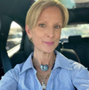 Woman wearing a blue striped shirt with visible jewelry, sitting inside a vehicle.