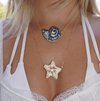Close-up of a necklace with a starfish pendant worn by a person in a white top.