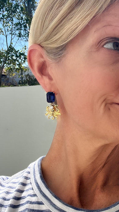 Close-up of a person wearing a blue earring with a gold flower design.