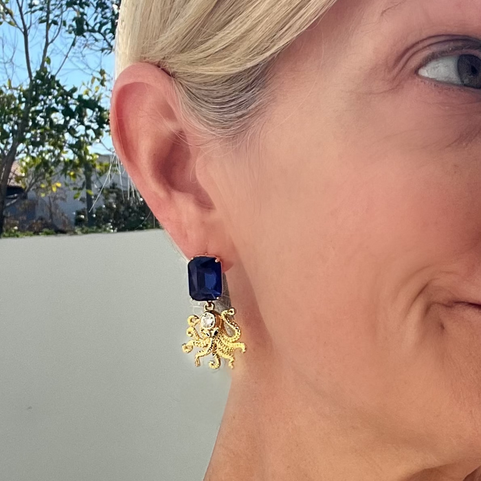 Close-up of a person wearing a blue earring with a gold flower design.