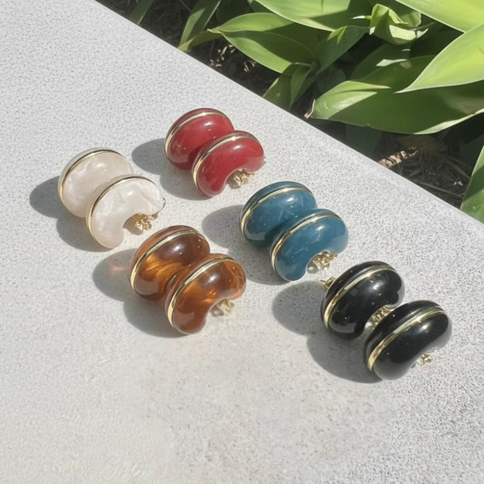 Set of colorful earrings on a light surface with green leaves in the background