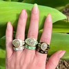 Hand wearing three decorative rings with green leaves in the background