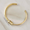A gold-colored twisted style bangle bracelet with an adjustable design, displayed on a marble surface.