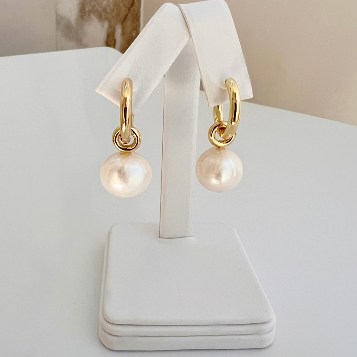 Gold hoop earrings with pearl drops on a white stand.