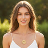 Woman wearing a gold necklace with a sunflower pendant against a blurred green background