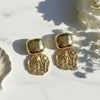 Gold earrings on a marble surface with floral background