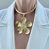 Gold flower-shaped necklace on a mannequin with a white jacket.
