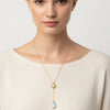 Woman wearing a gold necklace with a pendant on a plain background