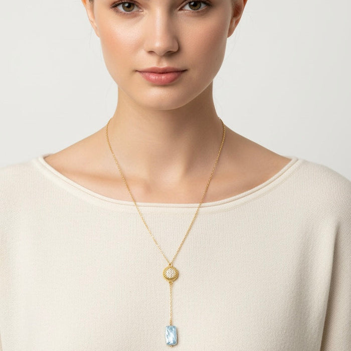 Woman wearing a gold necklace with a pendant on a plain background