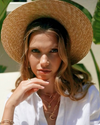 Woman wearing a straw hat and white shirt with gold jewelry outdoors
