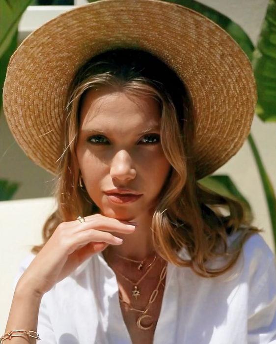 Woman wearing a straw hat and white shirt with gold jewelry outdoors