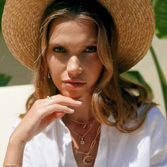 Woman wearing a straw hat and white shirt with gold jewelry outdoors