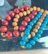 Three beaded bracelets in red, brown, and blue on a reflective surface.