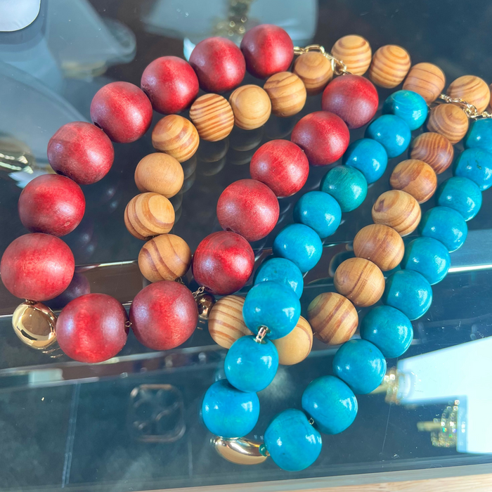 Three beaded bracelets in red, brown, and blue on a reflective surface.