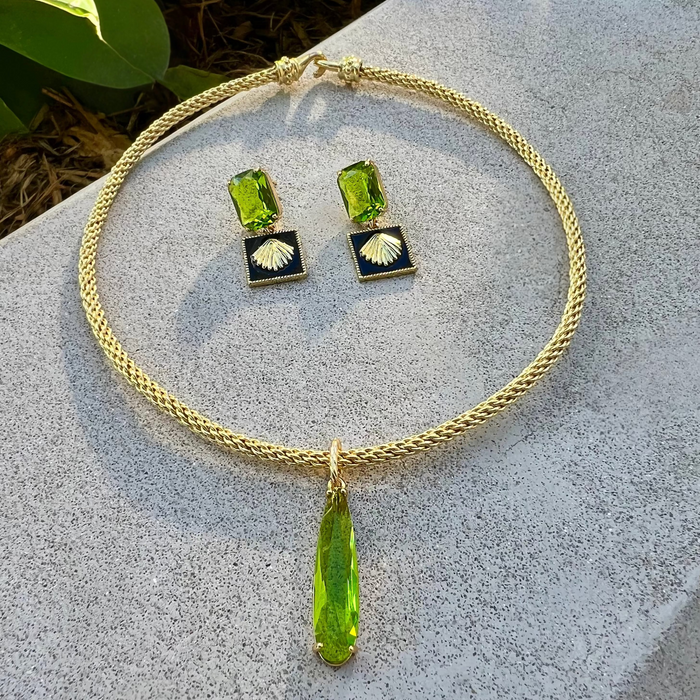 Gold necklace with green pendant and matching earrings on a stone surface.