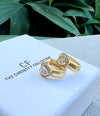 Gold earrings with heart-shaped gemstones on a branded box with green leaves in the background