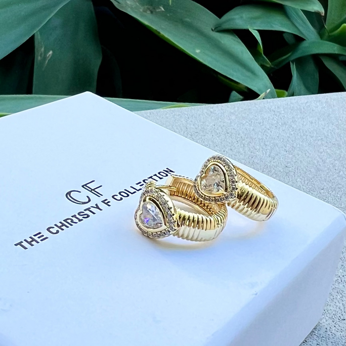 Gold earrings with heart-shaped gemstones on a branded box with green leaves in the background