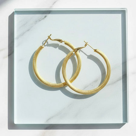 Gold hoop earrings on a white marble surface