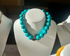 Turquoise beaded necklace on a white mannequin bust with other jewelry in the background.